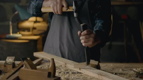 Carpenter, Shop worker In process Holds a chisel and hammer works with wood In the shop In slow