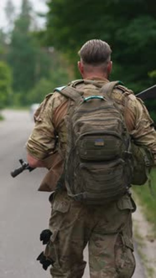 The Military Operative Equipped with a Weapon and a Backpack is Moving on the Road