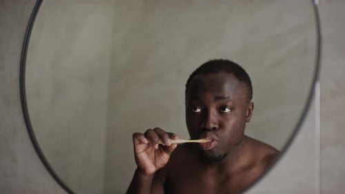 Young Black Man Brushing Teeth in Front of Mirror in Bathroom