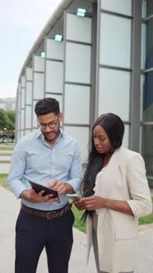Vertical video of two diverse Business colleagues using digital tablet outside office building