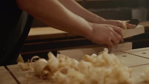 Hands planing wood with shavings on workbench in carpentry workshop