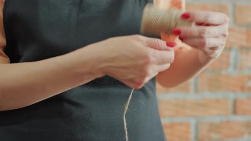 Florist in Black Apron Stretches Twine Spool with Hands