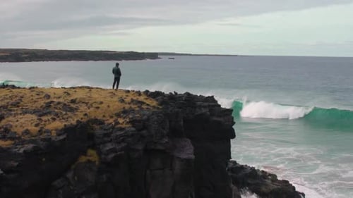 Man watches the waves rolling in and out from a cliff in slow motion