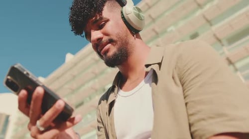 Close up, young student sits outside next to the university, listens to music on headphones