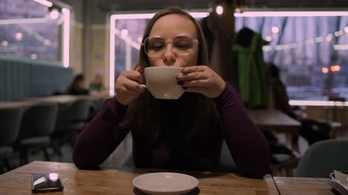 A Woman is Seated at a Table Holding a Cup of Coffee in the Cafe She Appears to Be Enjoying Her