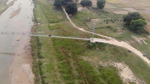 Aerial: motorbike crossing suspension bridge over a polluted river