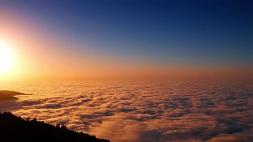 Setting sun colors the thick cloudscape covering the scenery among the mountains.