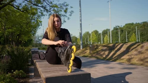 young beautiful girl in park tying laces on roller skates before skating workout active lifestyle