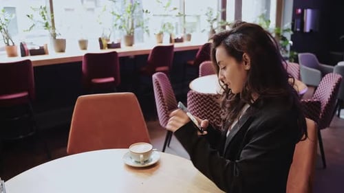 Caucasian Girl Drinking Cappuccino Inside of Cafe Female is Sitting at Round Table in the Middle of