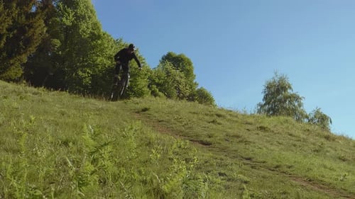 A MTB E-biker biking down the hill in the nature. Extreme rider is making jump trick.