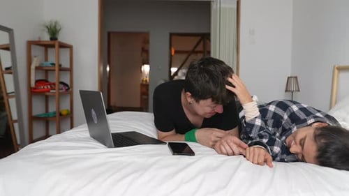 Friends Laughing Together in Bedroom With Laptop