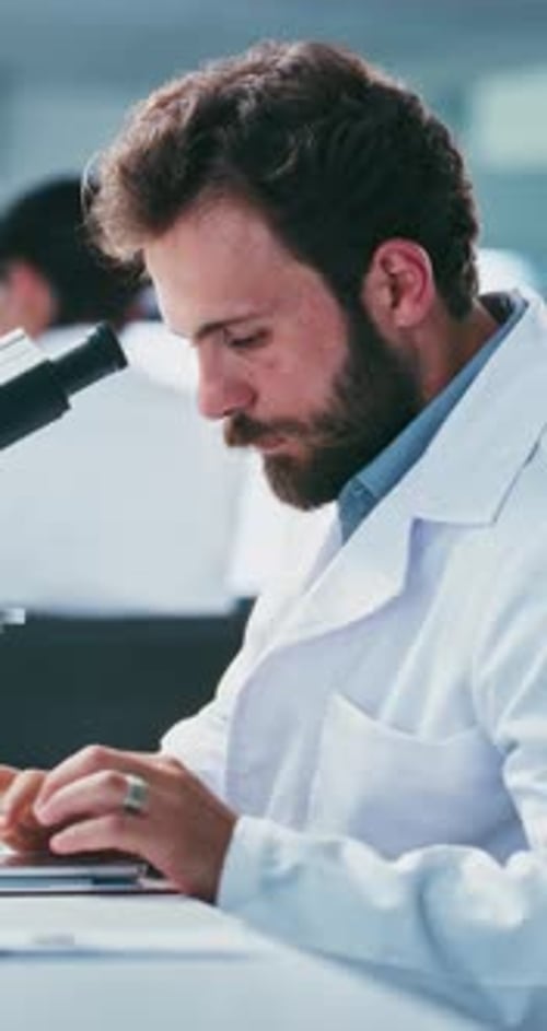 Man in Lab Coat Looks Through Microscope