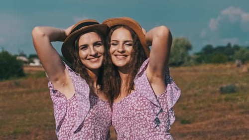 Retrato de dos jóvenes gemelas sonrientes con vestidos mirando a la cámara en la naturaleza