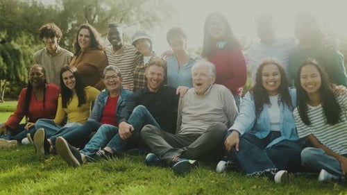 Happy multigenerational people with different ethnicity having fun sitting on grass in a public park