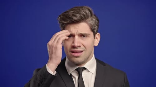 Stressed Man in Suit Massaging Temples Against Blue