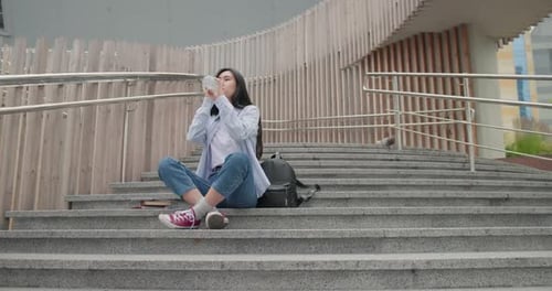 Woman Relaxing on Urban Stairs, Drinking Water