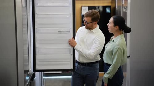 Salesman Helping Young Woman Choosing Fridge in Appliance Store
