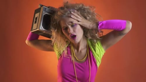 Young woman in 80s clothes, with a boombox on her shoulder, going crazy to the music
