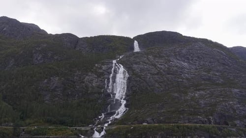 Boat approaches powerful Langfossen waterfall in Norwegian landscape