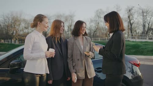 A Group of Business Women are Standing Near a Car and the Girl Boss is Handing Out Cash Bonuses to