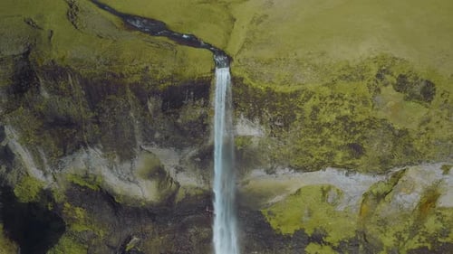 Aerial view of the scenic blue transparent waterfall at the mountain edge, surrounded by moss.