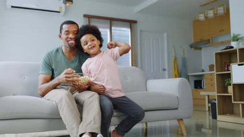 Man and Boy Cheering at Television Indoors