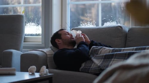 Homme caucasien malade allongé sur un canapé recouvert d'une couverture, virus de la grippe saisonnière, vaccin au ralenti