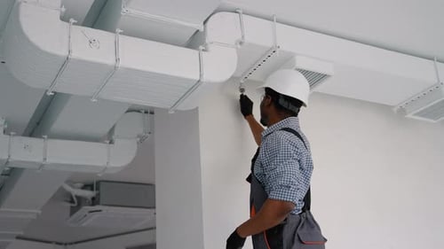 African Worker Install Ducted Pipe System for Ventilation and Air Conditioning in Office