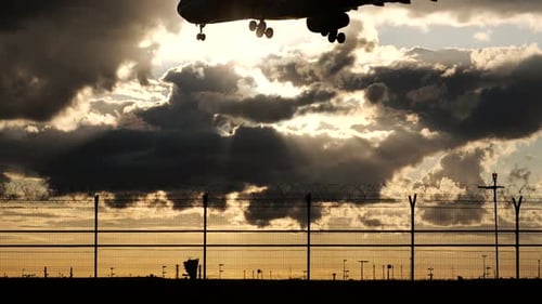 Airplane Landing at Sunset Behind Airport Fence
