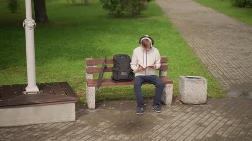 Man Waiting Outside Casual Student Sits Patiently on Park Bench Under Gray Sky Quiet Commuter with