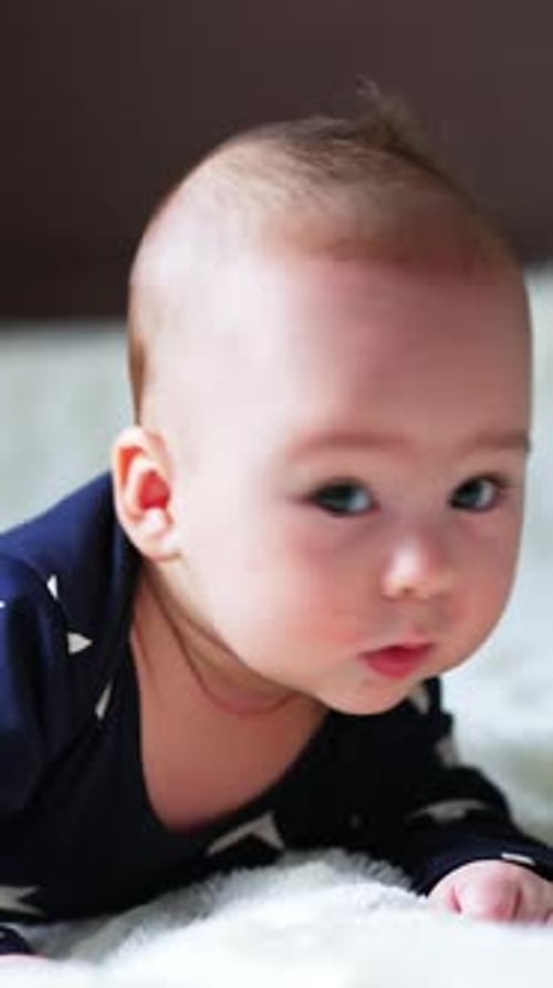 Little newborn baby looks puzzled gazing aside. Beautiful boy lies on belly keeping head up.