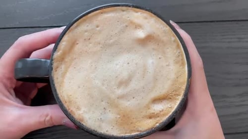 Hand holding a cup of hot pumpkin spice coffee latte.