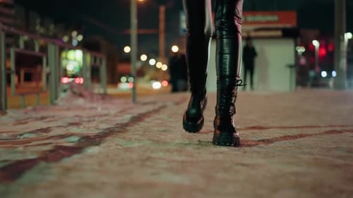 Woman Walking in Black Leather Trousers and Boots at Night on Snowy Street