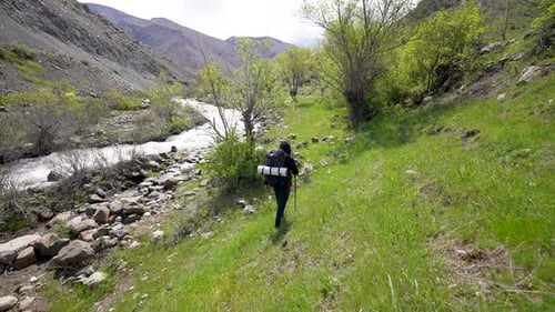 Hiker with Backpack Trekking Down Grassy Mountain Hill