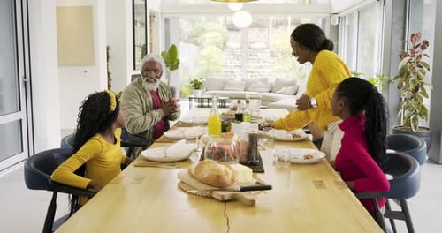 When Black mother entering with tray, diverse family placing dishes at dining table prepping meal