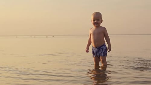 Cute Infant Standing in Water on Beach at Sunset