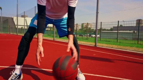 A tall guy basketball player throws a ball into a basketball hoop at a basketball court in the park