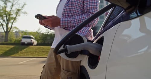 Electric Car Charging While Adult Uses Phone