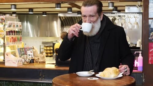 Elderly Man Enjoying a Warm Coffee and Fresh Croissant in a Cozy Cafe Setting