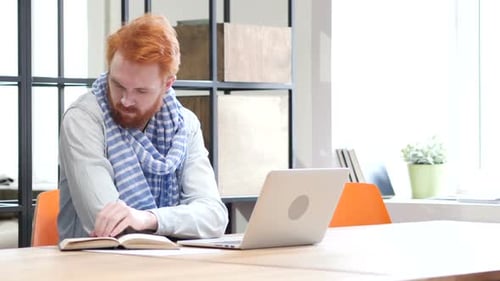 Man Reads Book and Types on Laptop