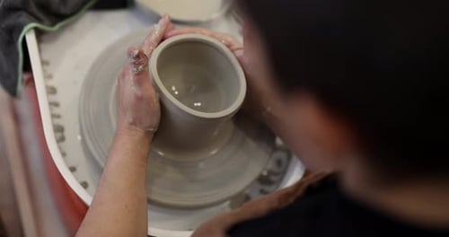 Des mains de potier professionnel façonnent habilement un bol en céramique sur un tour de poterie rotatif dans une caisse