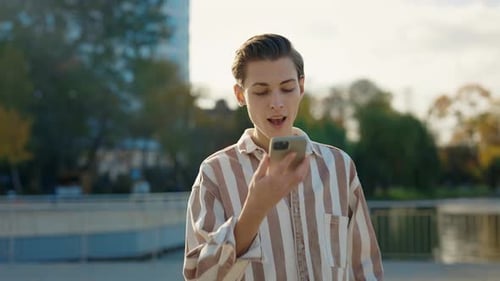 Young Caucasian Man in Casual Clothes Recording Voice Message Via Smartphone While Walking in City