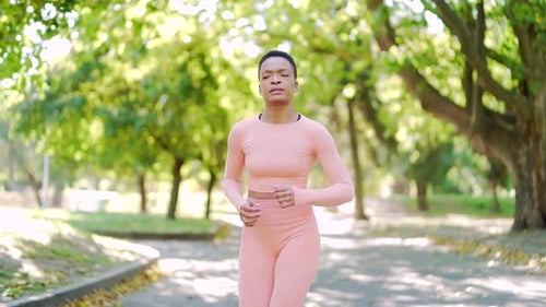 young african american slim woman runner jogging in the morning on urban park in pink tracksuit.