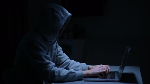 Gefährlicher männlicher Hacker mit Sweatshirt, der das Computersystem kaputt macht und ein Passwort zum Hacken eingibt