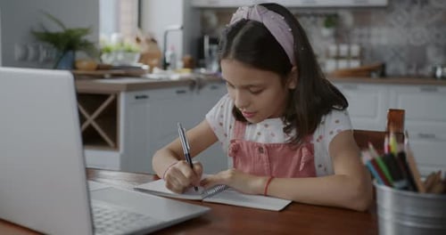Girl Studies with Laptop and Notebook in Kitchen