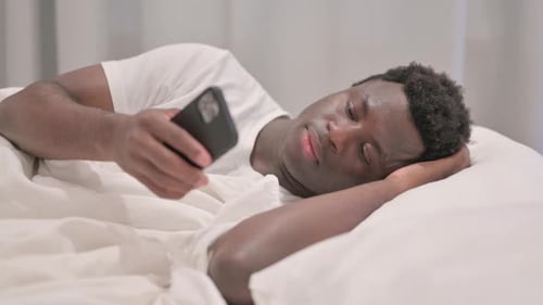 Man Lies in Bed, Looking at Smartphone