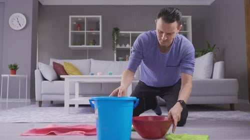 Man holding bucket under leaky ceiling and mopping floors.