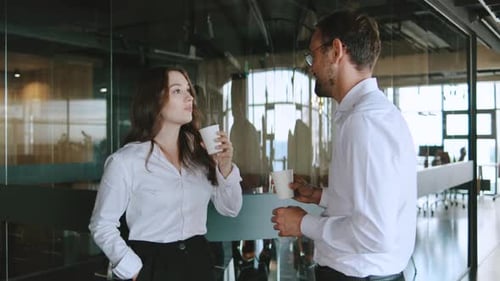People Talking in a Modern Office During a Coffee Break While Holding Cups and Standing Near Glass