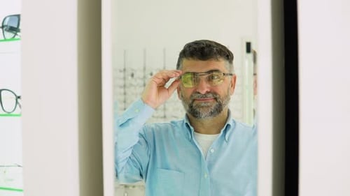 Un hombre que elige unas gafas nuevas de los años 50 y 60 en una tienda de óptica mirándose al espejo