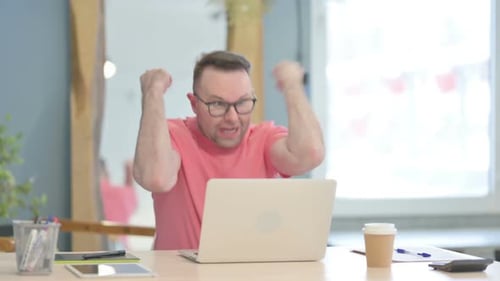 Man Cheering Success While Using Laptop in Office